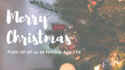 The Nimble Ape logo (a black ape with a white face in the shape of an A) is in the top right-hand corner of the page. Below, white text reads "Merry Christmas from all of us at Nimble Ape Ltd". The background image is a close up of a Christmas tree with a stocking decoration that reads Noel. In the bottom right-hand corner, a wooden arrow wearing a santa hat directs to the next image.