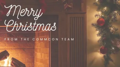 The CommCon logo sits in the top left-hand corner of the image. Below, text reads "Merry Christmas from the CommCon team". The image background is a cosy fireplace with festive garland. There is a gingerbread cookie arrow in the bottom right-hand corner pointing to the next image.